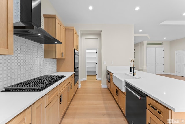 kitchen with wall chimney range hood, sink, light hardwood / wood-style flooring, tasteful backsplash, and black appliances