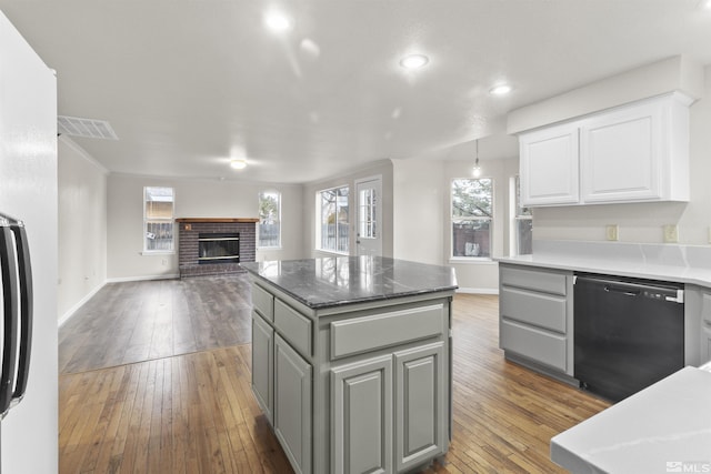 kitchen featuring a kitchen island, dishwasher, wood-type flooring, white cabinets, and a brick fireplace