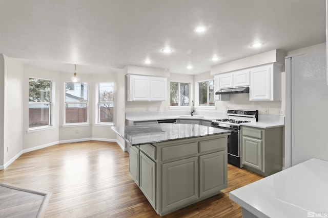 kitchen with range with gas stovetop, decorative light fixtures, white cabinetry, sink, and a center island