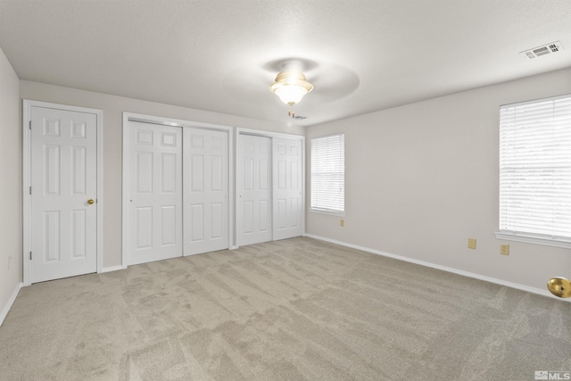 unfurnished bedroom with multiple windows, light carpet, and multiple closets