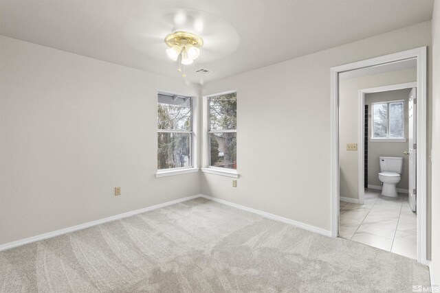 unfurnished bedroom with multiple windows, light colored carpet, and ensuite bath