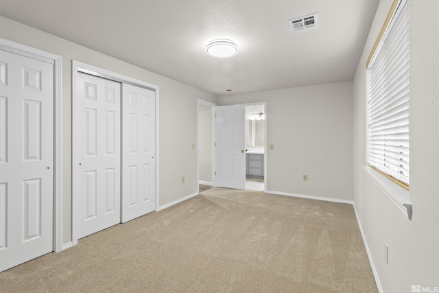 unfurnished bedroom with light carpet, ensuite bath, and a closet