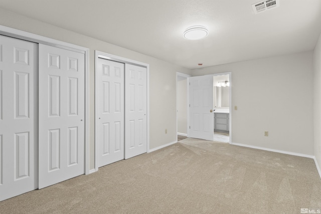 unfurnished bedroom featuring connected bathroom, light carpet, and two closets