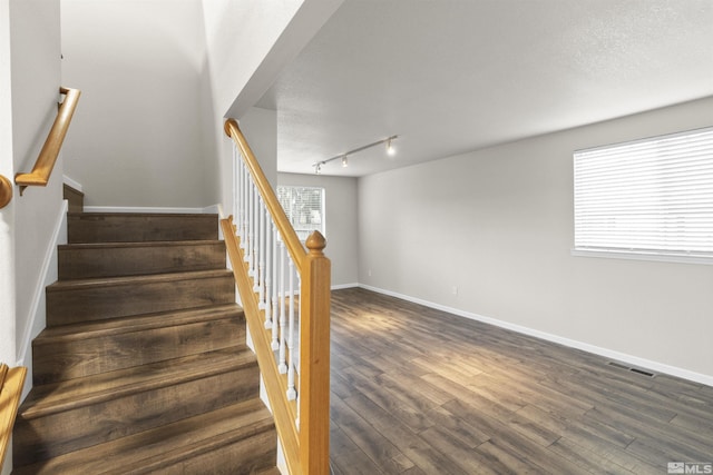 staircase with rail lighting, hardwood / wood-style floors, and a textured ceiling