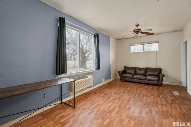 sitting room with a wall unit AC, light hardwood / wood-style floors, and ceiling fan