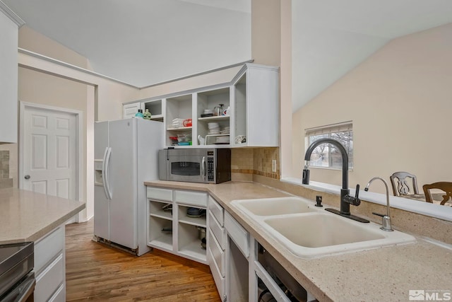 kitchen featuring sink, vaulted ceiling, light wood-type flooring, white fridge with ice dispenser, and white cabinets