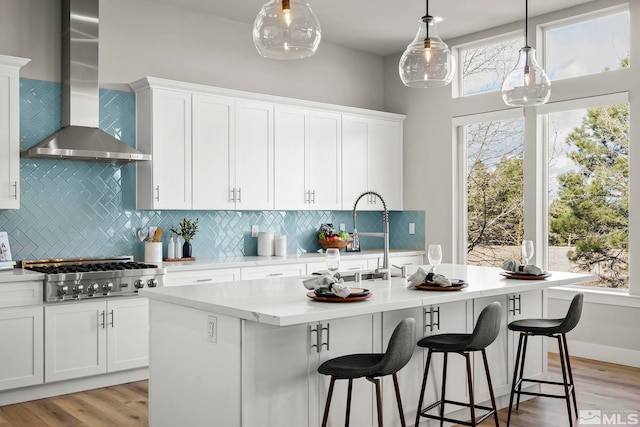 kitchen featuring white cabinetry, wall chimney exhaust hood, and a kitchen island with sink