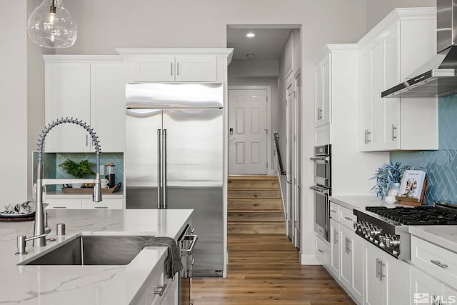 kitchen featuring wall chimney range hood, hardwood / wood-style flooring, appliances with stainless steel finishes, white cabinetry, and light stone counters