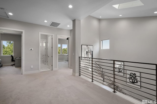 hall with plenty of natural light, light colored carpet, and a skylight