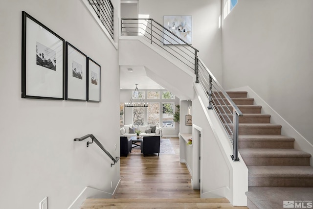 stairs with a notable chandelier, a towering ceiling, and hardwood / wood-style flooring