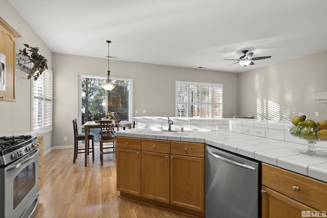 kitchen featuring tile counters, stainless steel appliances, decorative light fixtures, and light hardwood / wood-style floors