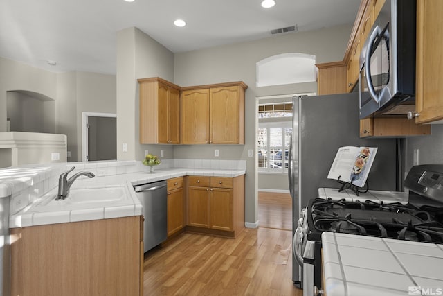 kitchen with sink, stainless steel appliances, tile counters, kitchen peninsula, and light wood-type flooring