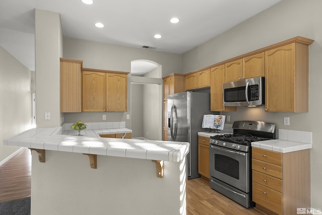 kitchen featuring appliances with stainless steel finishes, tile countertops, a kitchen breakfast bar, and kitchen peninsula