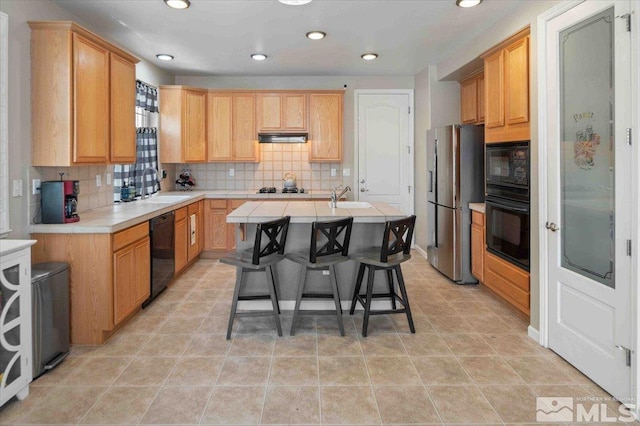 kitchen featuring sink, tasteful backsplash, black appliances, a center island with sink, and exhaust hood