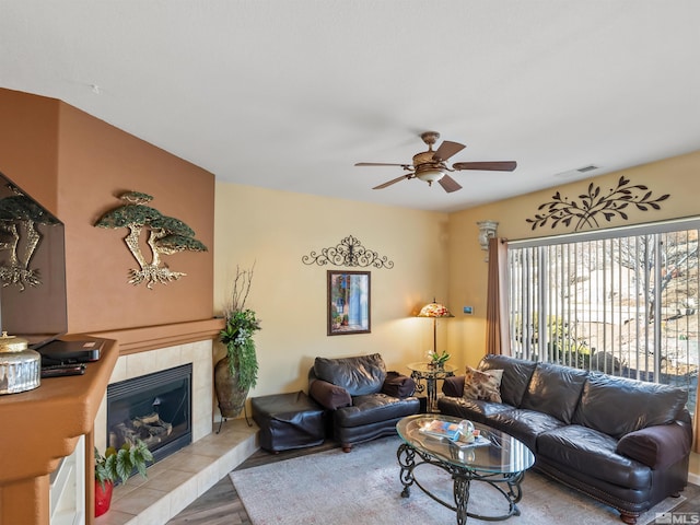 living room featuring a tile fireplace, ceiling fan, and light hardwood / wood-style flooring