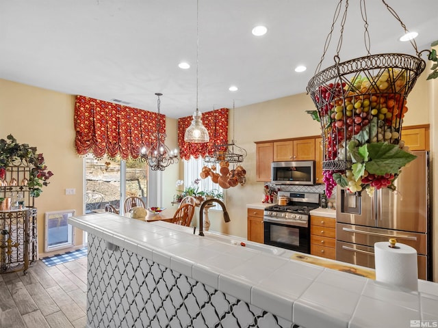 kitchen with appliances with stainless steel finishes, hardwood / wood-style floors, tile countertops, decorative backsplash, and hanging light fixtures