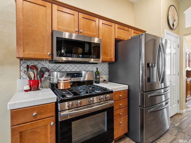 kitchen with tasteful backsplash, appliances with stainless steel finishes, tile counters, and light wood-type flooring