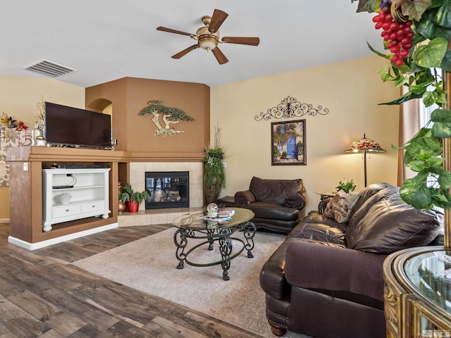 living room featuring ceiling fan, a tiled fireplace, and hardwood / wood-style floors