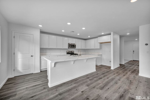 kitchen with appliances with stainless steel finishes, white cabinets, light stone counters, a center island with sink, and light hardwood / wood-style flooring