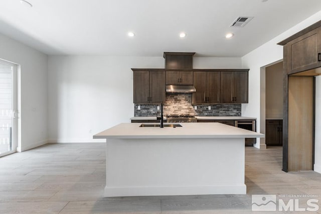 kitchen with dark brown cabinetry, sink, a kitchen island with sink, and decorative backsplash