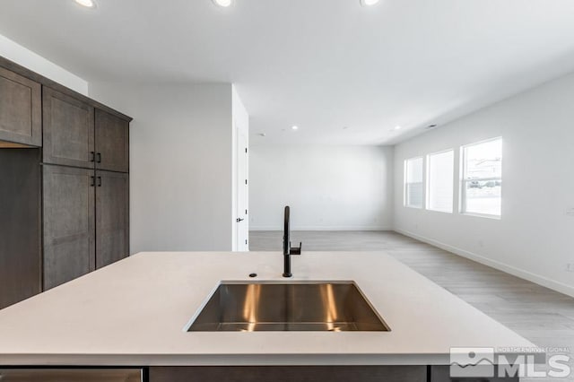 kitchen featuring dark brown cabinetry, an island with sink, sink, and light hardwood / wood-style flooring