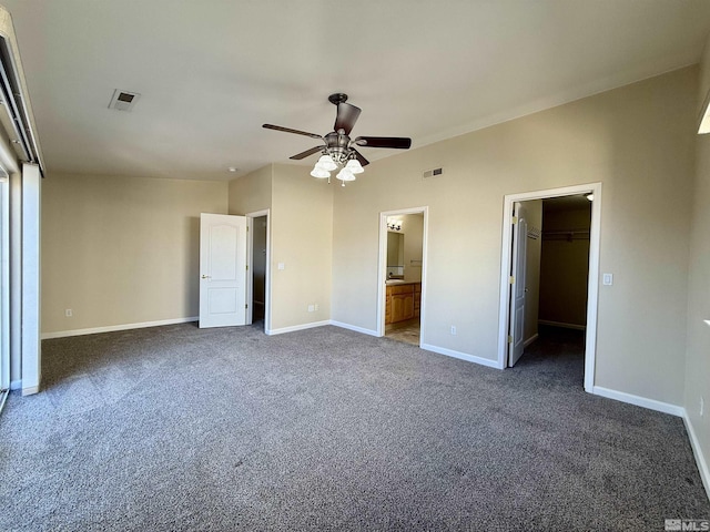 unfurnished bedroom featuring ceiling fan, connected bathroom, dark carpet, a walk in closet, and a closet