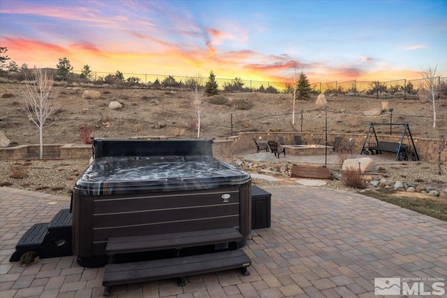 patio terrace at dusk featuring a fire pit and a hot tub