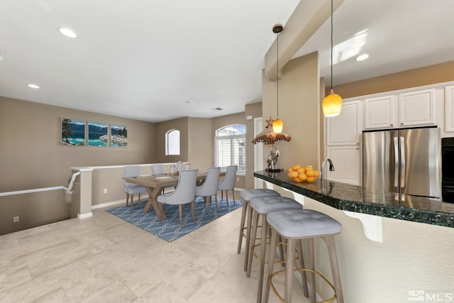 kitchen with decorative light fixtures, a kitchen breakfast bar, stainless steel fridge, dark stone counters, and white cabinets