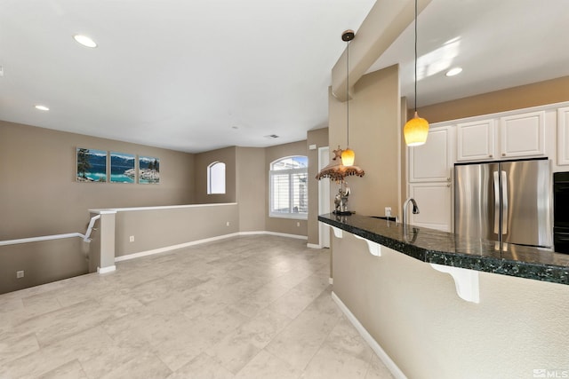 kitchen featuring sink, white cabinetry, decorative light fixtures, dark stone countertops, and stainless steel refrigerator