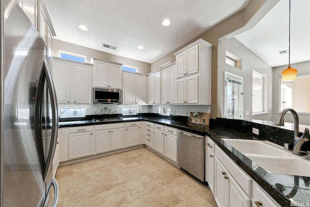 kitchen with sink, appliances with stainless steel finishes, dark stone countertops, hanging light fixtures, and white cabinets