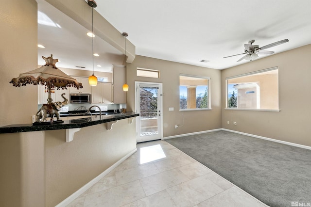 kitchen with a kitchen bar, hanging light fixtures, kitchen peninsula, light colored carpet, and white cabinets