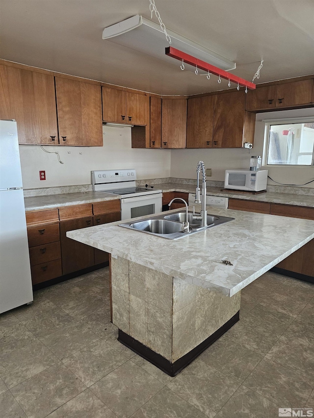 kitchen with a kitchen island with sink, a sink, white appliances, brown cabinets, and light countertops