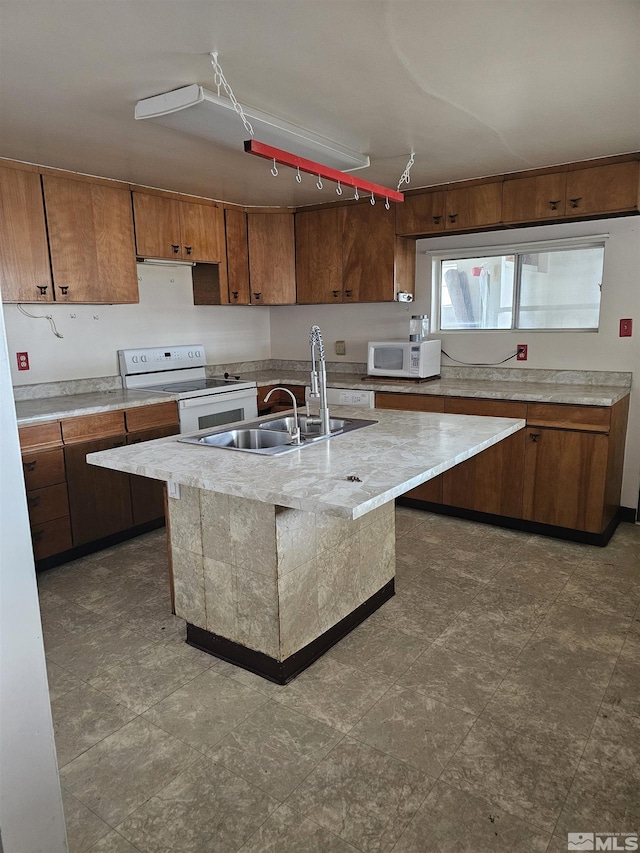 kitchen featuring brown cabinets, light countertops, a sink, white appliances, and a center island with sink