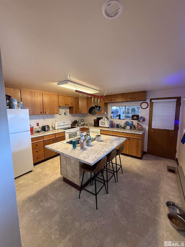 kitchen featuring a sink, brown cabinets, a kitchen island with sink, white appliances, and light countertops