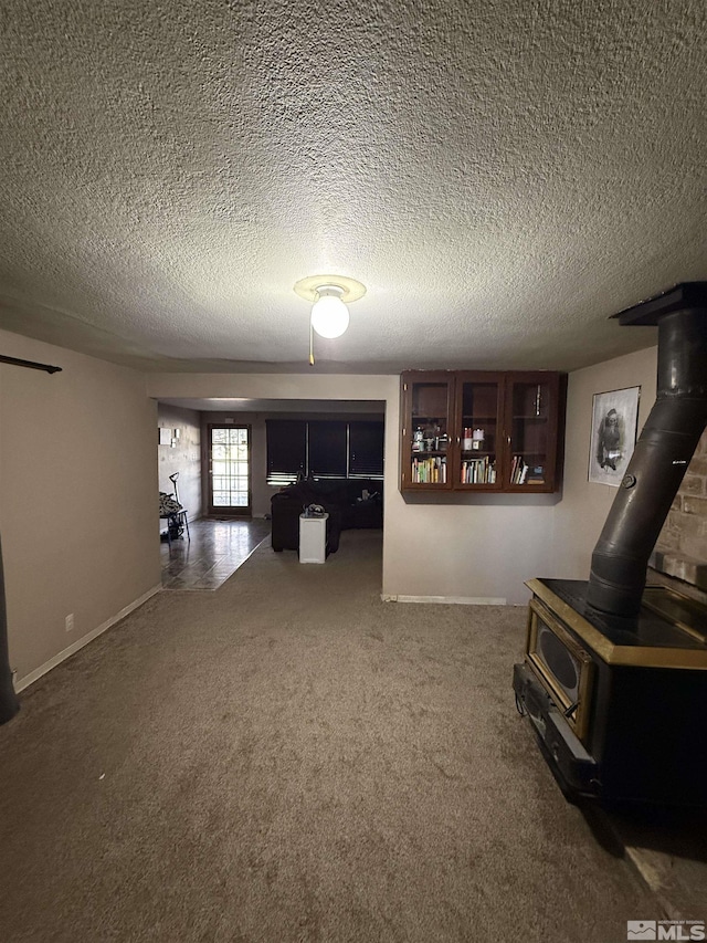 unfurnished living room with carpet flooring, a textured ceiling, and a wood stove