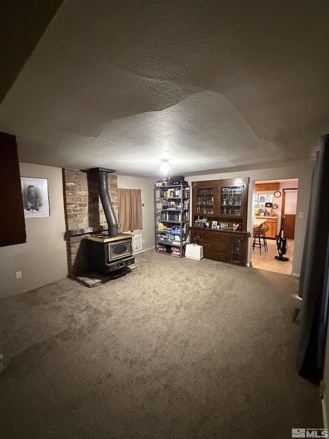 interior space featuring carpet flooring, a textured ceiling, and a wood stove