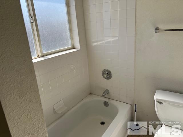 bathroom with tiled shower / bath combo and toilet