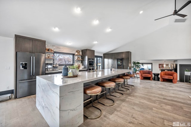 kitchen featuring stainless steel fridge, a breakfast bar area, a spacious island, dark brown cabinetry, and vaulted ceiling