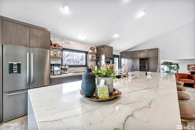 kitchen with a breakfast bar, appliances with stainless steel finishes, a kitchen island with sink, dark brown cabinets, and vaulted ceiling