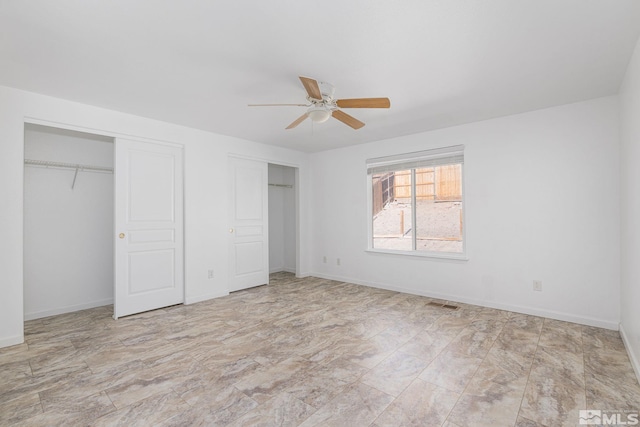 unfurnished bedroom featuring ceiling fan and two closets