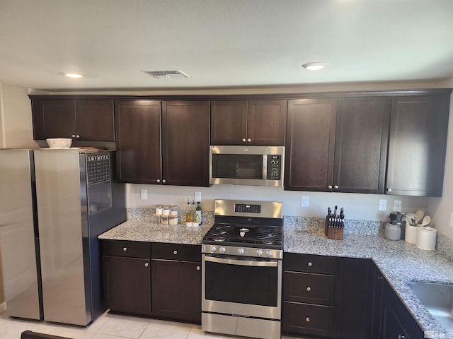 kitchen featuring appliances with stainless steel finishes, dark brown cabinets, light tile patterned floors, and light stone counters