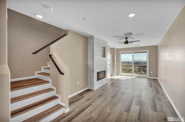 unfurnished living room featuring ceiling fan, a tiled fireplace, and light hardwood / wood-style flooring