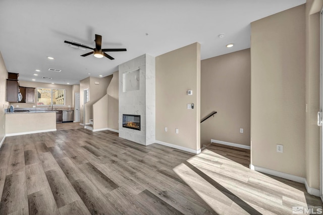 unfurnished living room with ceiling fan, a tiled fireplace, sink, and light hardwood / wood-style flooring