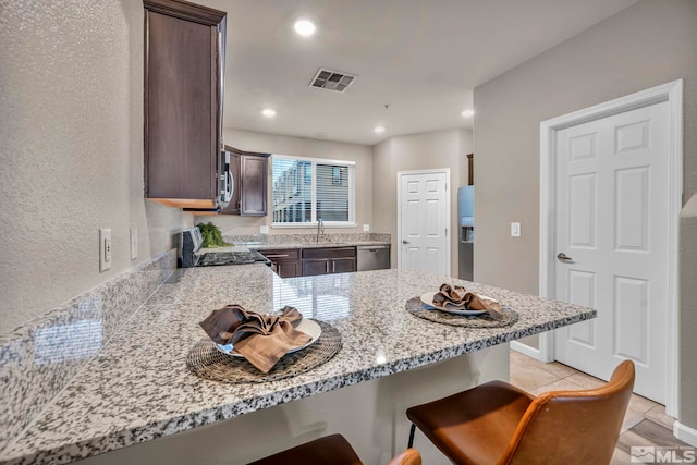 kitchen with dark brown cabinetry, sink, a breakfast bar, and appliances with stainless steel finishes