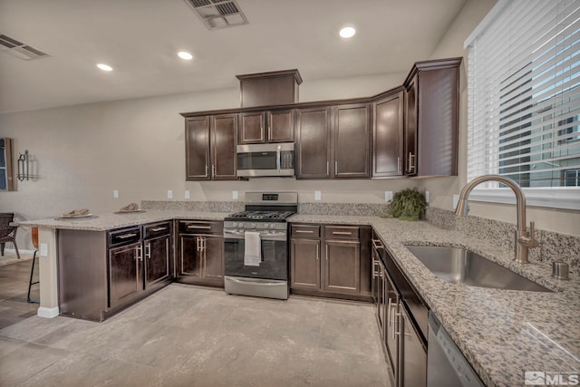 kitchen with light stone counters, stainless steel appliances, kitchen peninsula, and sink