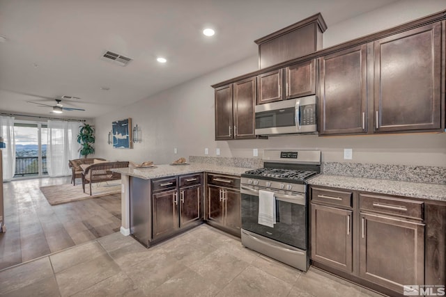 kitchen with dark brown cabinetry, light stone counters, kitchen peninsula, ceiling fan, and stainless steel appliances