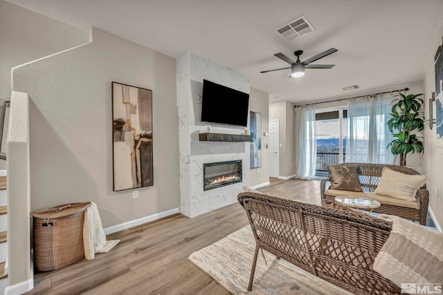 living room with a fireplace, ceiling fan, and light wood-type flooring