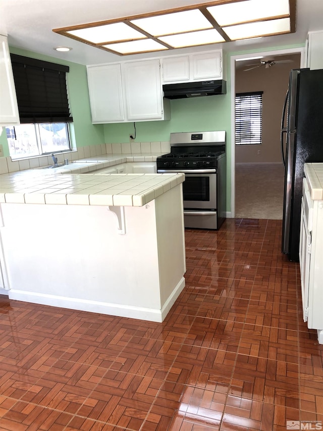 kitchen featuring stainless steel gas range, black refrigerator, white cabinets, tile countertops, and kitchen peninsula