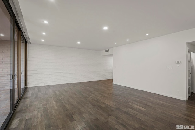 unfurnished room featuring dark hardwood / wood-style flooring and brick wall