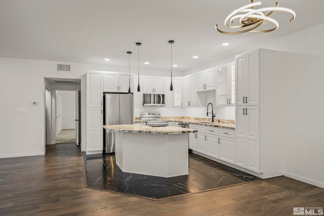 kitchen featuring decorative light fixtures, stainless steel appliances, white cabinets, and a kitchen island